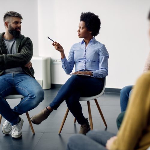 African American female therapist talking to a man during group counselling.