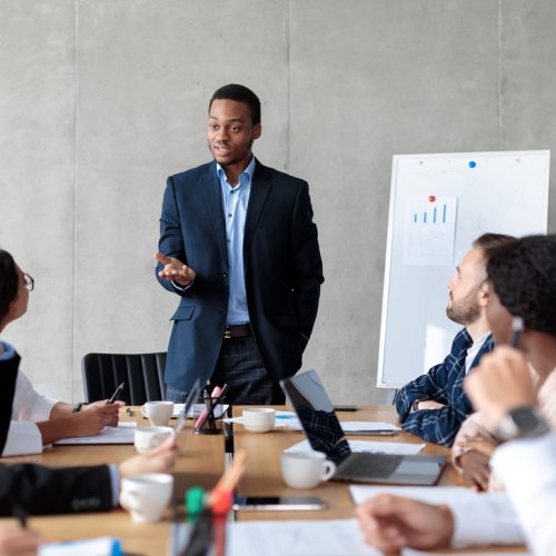 Discontented African Businessman Giving Speech During Corporate Meeting With Employees Displeased With Results Of Their Work In Modern Office. Selective Focus, Panorama